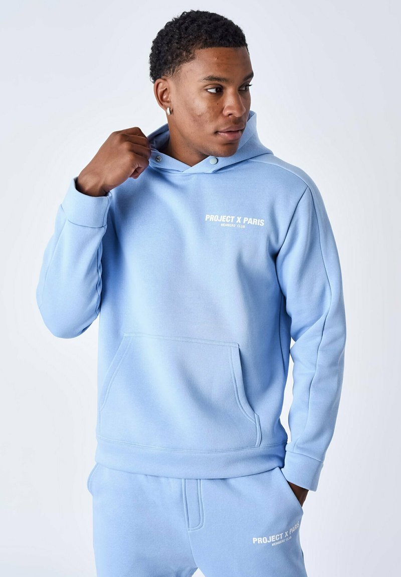 Sudadera con capucha de color azul claro, hecha de un tejido suave, que presenta un bolsillo frontal y una marca en texto blanco en el pecho y los pantalones.