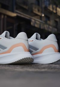 Paire de chaussures de running blanches avec des accents pêche sur une surface en béton, sur un fond urbain flou.