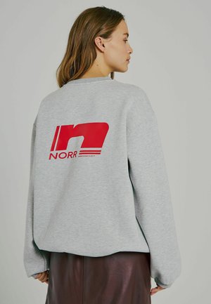 Pilkas megztinis su laisvu kirpimu, ant nugaros turintis didelį raudoną grafiką "n" ir "NORR" logotipą. Minkšta medžiaga su ribotais rankogaliais.