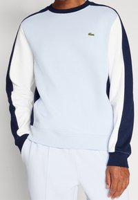 Felpa azzurra chiara con maniche navy e bianche, colletto a coste, e logo ricamato sul petto. Realizzata in morbido tessuto di cotone.