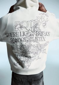 Felpa bianca con un intricato grafica di vite nera e design testuale sul retro. Il materiale sembra morbido, con una vestibilità comoda e cappuccio con coulisse.