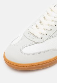 Baskets blanches avec tige en cuir texturé et en daim, lacets blancs et semelle en caoutchouc gomme, vues de l'angle avant latéral.