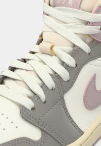 Suurem plaan hallist, valgest ja roosast Nike Air spordijalatsist, kus on näha valged paelad, õmblused ja roosa Nike logo jalatsi küljel.