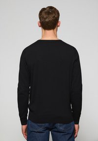 Jersey negro de manga larga con cuello redondo y puños acanalados, hecho de una tela suave. La parte trasera presenta un diseño simple y sin adornos.