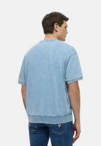 T-shirt oversize in cotone azzurro chiaro con maniche corte, scollo rotondo e cuciture grezze. La texture appare morbida e leggermente testurizzata.