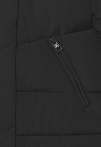 Černá péřová bunda, která ukazuje prošívanou strukturu, boční kapsu na zip s logem na stříbrném táhle, a hladký povrch látky.