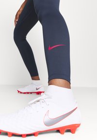 Marinblåa träningsleggings med en rosa Nike-logotyp, matchade med vita fotbollsskor med röda och silverakcenter samt en texturerad yta.