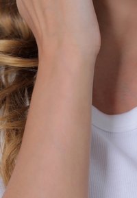 Gros plan sur l'avant-bras et le poignet d'une personne à la peau claire et aux cheveux blonds ondulés, portant une chemise blanche à côtes.