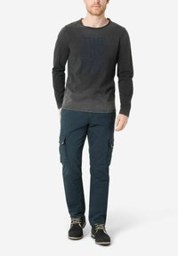 Long-sleeve dark gray shirt with blue text "TIME ZONE & CO," paired with teal cargo pants featuring side pockets and black shoes.
