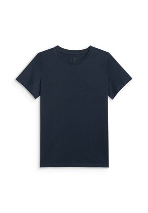 Chłopiec stoi z rękami za plecami, ubrany w granatowy t-shirt, zielone krótkie spodenki typu cargo, białe skarpetki i białe trampki, patrzy w bok.