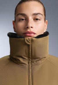 Brown high-collared jacket featuring a soft black fur lining at the collar. Smooth fabric with a seam detail down the center.