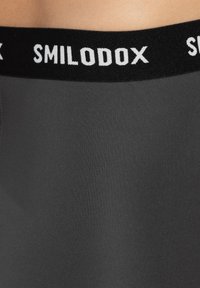 Grijze sportshorts met een zwarte elastische tailleband waarop de merknaam "SMILODOX" in witte letters is gedrukt. Glad, aansluitend materiaal.