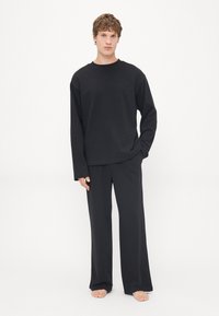 Zwarte longsleeve met bijpassende broek in een losse pasvorm. De stof lijkt glad met een matte textuur. Minimalistisch ontwerp, geen patronen of accenten.
