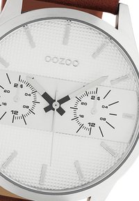 Silver analog watch with a textured white dial, black accents, three subdials, and a brown leather strap. Features bold hour markers.