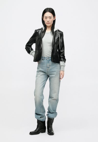 Μαύρο δερμάτινο τζάκετ με γκρι φούτερ, ανοιχτό γκρι μπλούζα, ανοιχτό μπλε τζιν και μαύρες μποτάκια στους αστραγάλους. Ματ υφές και εφαρμοσμένα σχεδιαστικά στοιχεία.