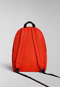 Mochila de lona roja con correas negras, forma redondeada y un asa superior. Presenta una textura suave y un diseño minimalista.