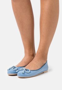 Jasnoniebieskie lakierowane baleriny z okrągłym czubkiem i ozdobnymi kokardkami z linijki. Płaska podeszwa z delikatnym beżowym wykończeniem.