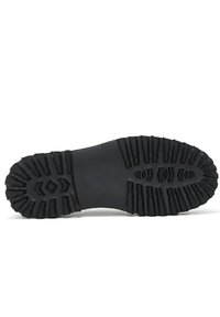 Semelle de chaussure en caoutchouc noir avec des motifs de traction profonds, comportant des formes en zigzag et hexagonales pour une meilleure adhérence. Zone centrale lisse avec des bords texturés.