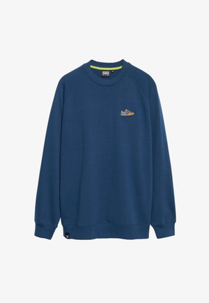 Tamno plavi dukserica od mješavine pamuka, s okruglim izrezom i rebrastim manžetama. Izdvojeni grafički prikaz tenisice u vibrantnim bojama na prsima.