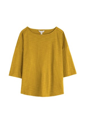 Haut ample jaune moutarde avec manches larges arrivant aux coudes et encolure ronde sur fond blanc.