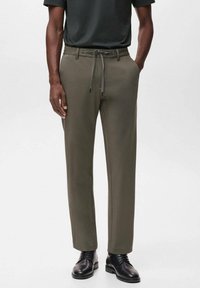 Olive green trousers in a tapered design with a drawstring waist, crafted from a smooth fabric, paired with black dress shoes.