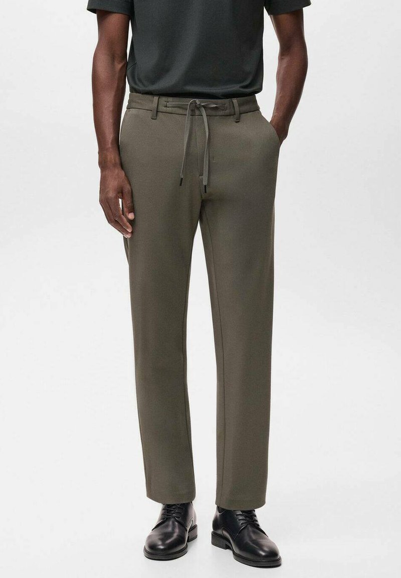Pantalons vert olive au design ajusté avec une taille à cordon, fabriqués dans un tissu lisse, associés à des chaussures habillées noires.