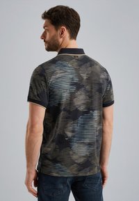 Polo avec un fond sombre, orné de lignes horizontales et de motifs abstraits en bleu et beige, à manches courtes et avec un col.