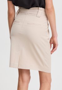 Beige pennkjol med en figurnära design, slättextur, sidofickor och en bältesöppning i midjan. Längd till mitten av låret.