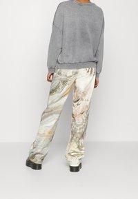 Szara bluza o luźnym kroju, zestawiona z wzorzystymi spodniami w jasnych kolorach i abstrakcyjnym, marmurkowym wzorze. Czarne obuwie.