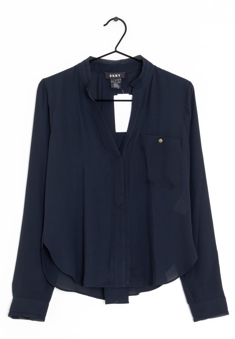 Blouse bleu marine foncé à manches longues avec col mandarin, poche poitrine avec bouton et étiquette, suspendue sur un cintre noir sur fond blanc.