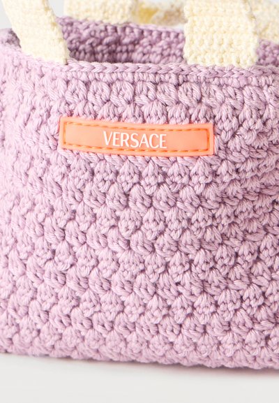 Πλεκτή τσάντα χειρός σε λιλά αποχρώσεις με εκρού λαβές και πορτοκαλί ετικέτα Versace στο μπροστινό μέρος.