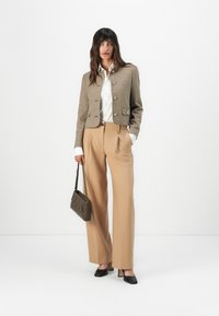 Giacca corta a quadri marrone, blusa bianca, pantaloni larghi color beige, tacchi neri, borsa grigia con motivo a zigzag, textures lisce.