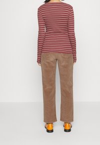 Långärmad marsala- och krämrandig skjorta i kombination med bruna kordflorsebyxor och orange skor, vy från baksidan.