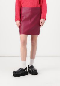 Fuchsia Leder Minirock mit glatter Textur, kombiniert mit klobigen schwarzen Plateau-Schuhen und weißen Knöchelstrümpfen. Darüber ein gestrickter rosa Pullover.