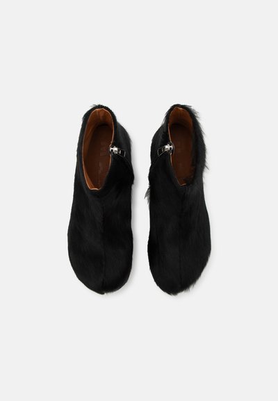 Czarne buciki slip-on z sztucznego futra z zaokrąglonym noskiem i srebrnym akcentem w postaci klamry. Gładkie wykończenie wnętrza oraz płaska podeszwa zapewniające dodatkowy komfort.