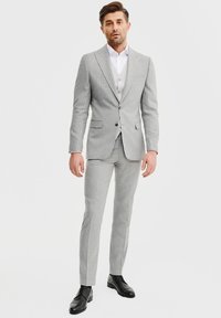 Jasnoszary garnitur w prążki składający się z dopasowanej marynarki i slim fit spodni, połączony z białą koszulą elegancką i szarym kamizelką. Czarne buty dopełniają stylizację.