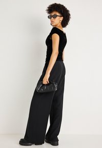 Μαύρη βελούδινη εφαρμοστή τοπ με κοντά μανίκια, μαύρο ψηλόμεσο παντελόνι με φαρδιά πόδια, χοντρές μαύρες πλατφόρμες και μια μικρή μαύρη τσάντα clutch.