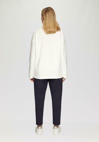 Witte oversized trui met verlaagde schouders, gecombineerd met donkerblauwe broeken. Opvallende details zijn de geribbelde zoom en de gestructureerde stof.