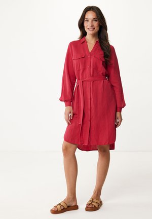 Robe rouge à boutons avec deux poches poitrine et une taille nouée, dotée de manches longues et d'un ourlet arrondi. Portée avec des sandales beiges.