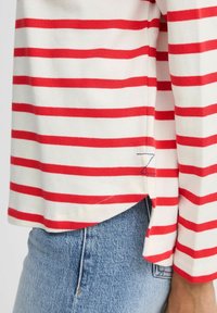 Langarmshirt aus weichem Baumwollstoff mit roten und weißen Streifen, das einen leichten seitlichen Schlitz und ein kleines gesticktes "Z"-Detail am Saum aufweist.