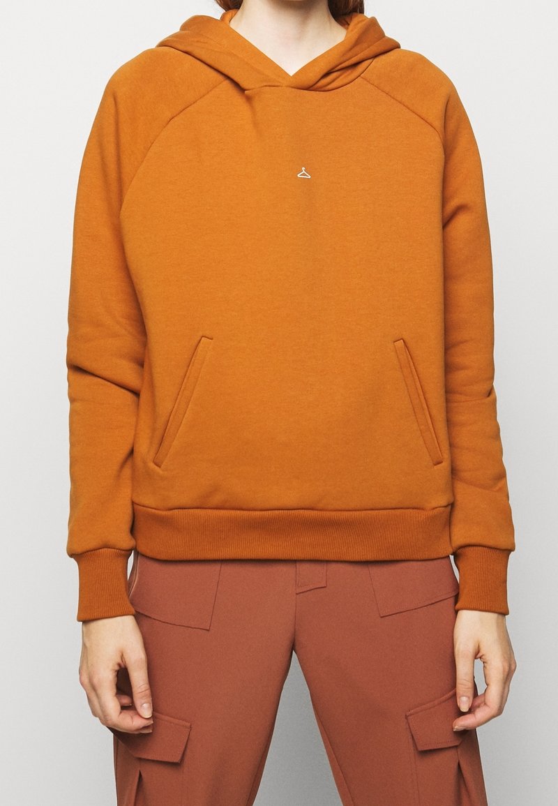 Sudadera con capucha naranja, mezcla de algodón, que presenta un pequeño logo blanco, puños acanalados y un bolsillo canguro. Textura suave, ajuste relajado.