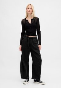 Top nero a coste a maniche lunghe con bottoni, abbinato a pantaloni neri a gamba larga con coulisse in vita e tasche laterali. Scarpe da ginnastica nere.