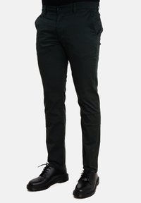 Chinos verde scuro con una vestibilità slim, caratterizzati da un frontale piatto, tasche laterali e chiusura con bottone. Abbinati a scarpe nere con lacci.