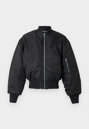 Black bomber jacket with front zipper, ribbed cuffs and hem, and zippered pocket on the left sleeve, displayed on white background.