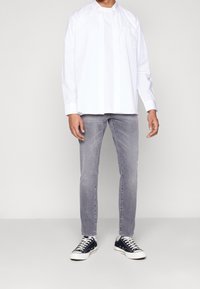 Bílá košile na knoflíky s kapsou, doplněná šedými úzkými džíny a tmavými teniskami. Jednoduchý design, lehká tkanina a neformální styl.