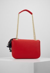 Punainen synteettinen käsilaukku, jossa on sileä pinta, suorakulmainen muoto, kultaketjuolkaimeen ja koristeellinen huiviakseli.