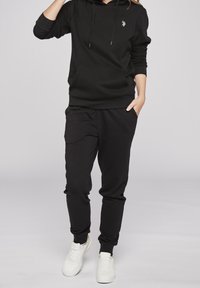 Svart hoodie med en framficka och dragsnören. Kombinerad med svarta sweatpants. Bärs med vita sneakers. Mjuk, avslappnad textur.