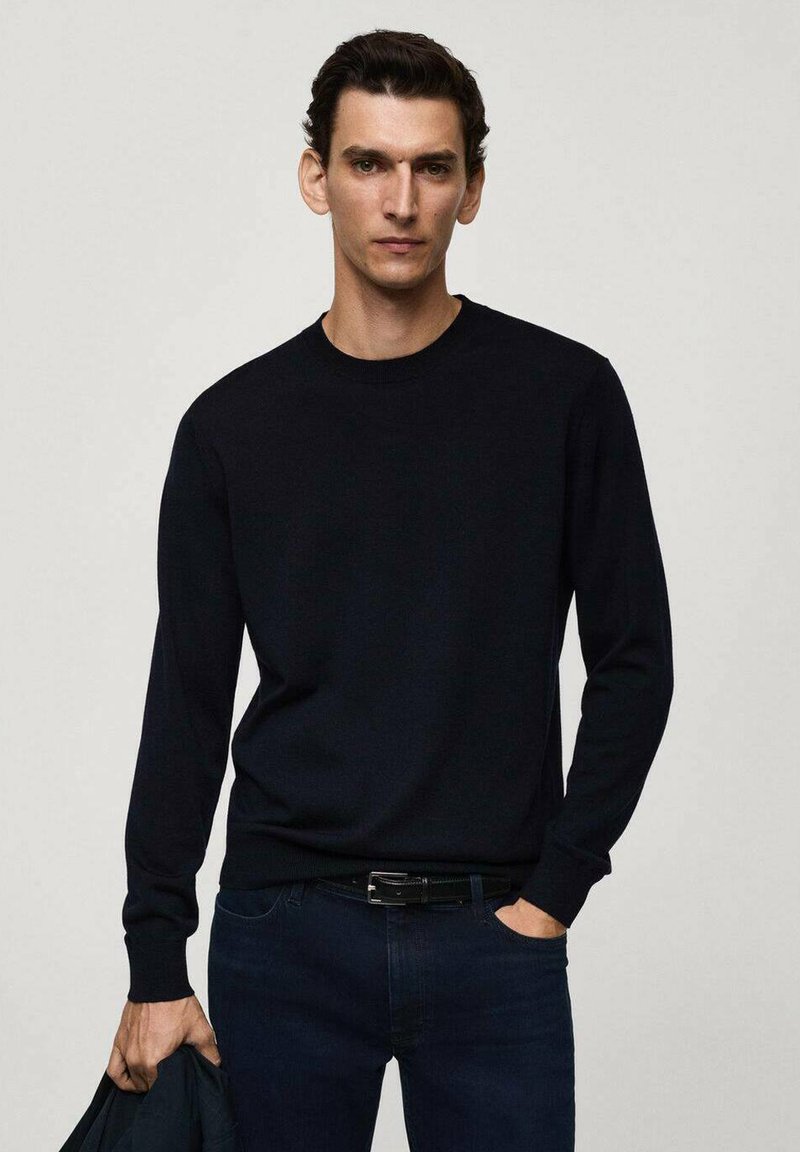 Sweater girocollo blu navy realizzato in materiale a maglia con maniche lunghe. Presenta un colletto e polsini a coste. Indossato sopra jeans scuri.