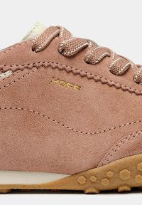 Zapatilla de ante rosa claro con superficie texturizada, acentos de cuero blanco contrastante y un logo dorado "HOFF" cerca de los cordones. Patrón hexagonal en la suela exterior.