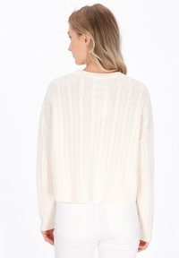 Maglione a maglia a disposizione di crema con design cropped e polsini a coste. Il tessuto è morbido e testurizzato, con un ampia scollatura e una vestibilità rilassata.